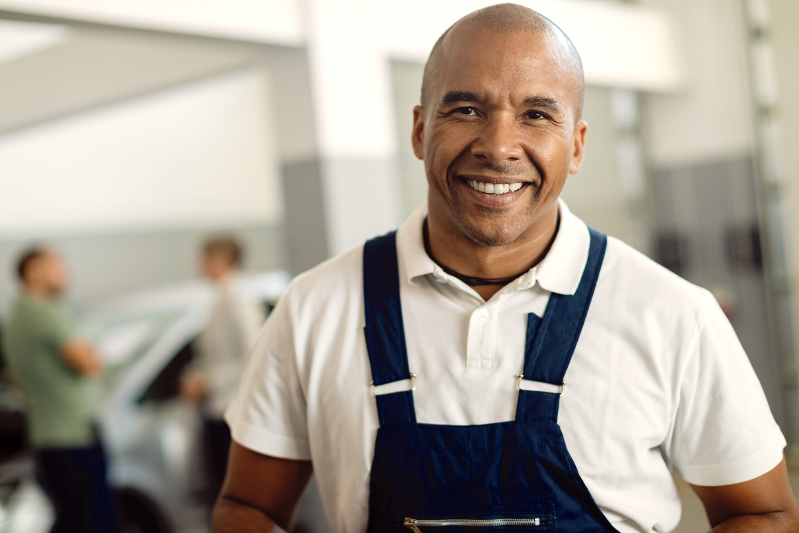 Homem sorridente em uniforme de trabalho, representando um profissional de serviços com ambiente de escritório ao fundo, promovendo confiança e qualidade.